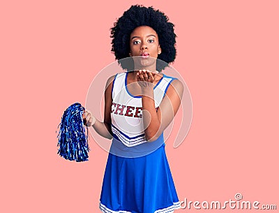 Young african american woman wearing cheerleader uniform holding pompom looking at the camera blowing a kiss with hand on air Stock Photo