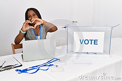 Young african american woman working at political election sitting by ballot smiling in love doing heart symbol shape with hands Stock Photo