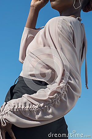 Young african black model posing showing details of a white blouse. Fashionable shot against a blue sky Stock Photo