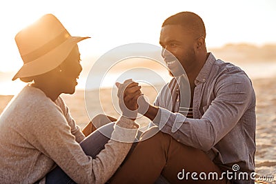 Young African couple sitting together on a beach at sunset Stock Photo