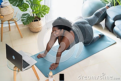 Young African curvy woman doing pilates virtual fitness class with laptop at home Stock Photo