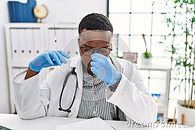 Young african doctor man holding syringe at the hospital tired rubbing nose and eyes feeling fatigue and headache Stock Photo