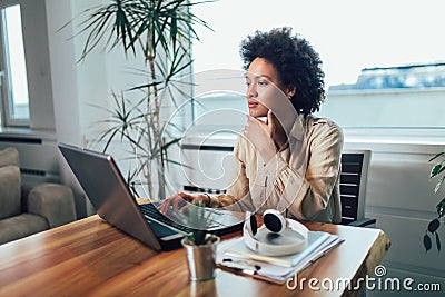 Young African female entrepreneur sitting at a desk in her home office working online with a laptop Stock Photo