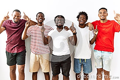Young african group of friends standing together over isolated background smiling amazed and surprised and pointing up with Stock Photo