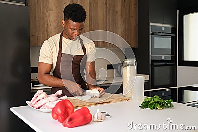 Young african man cutting onion to prepare chicken recipe. Stock Photo