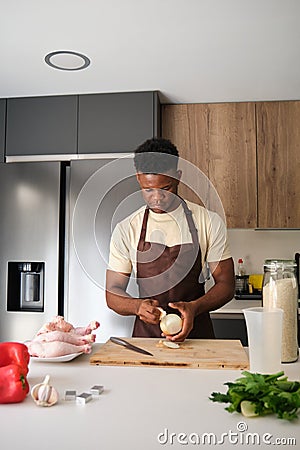 Young african man peeling onion to prepare chicken recipe. Stock Photo