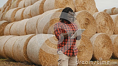 Young african man,working on tablet in front of the hay roll stack. Smart farming concept Stock Photo