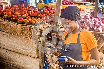 african woman selling in a local african market holding a mobile point of sale system and using her mobile phone Stock Photo