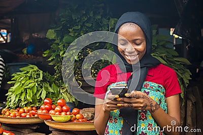 Young african woman selling in a local market smiling while using her mobile phone Stock Photo