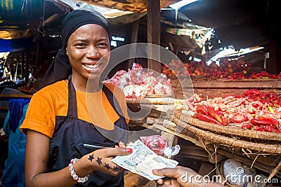 Young african woman selling food stuff in a local african market collecting money from a paying customer Stock Photo