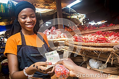 Young black woman selling food stuff in a local african market collecting money from a paying customer Stock Photo