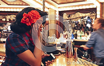 Young afro 1950s dressed woman at the bar counter of a aright carnival fair style bar at the Flight Cub, a vintage Editorial Stock Photo