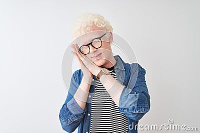 Young albino blond man wearing denim shirt and glasses over isolated white background sleeping tired dreaming and posing with Stock Photo
