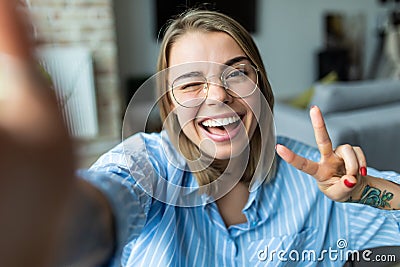 Young amazing emotional pretty lady lies on sofa indoors looking camera make selfie make peace gesture Stock Photo