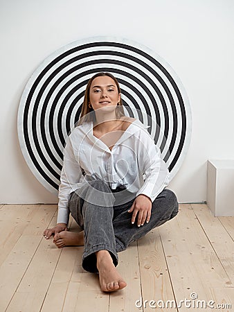 Young ambitious brunette, concept. Young woman sitting on the floor against a background of concentric circles, Stock Photo