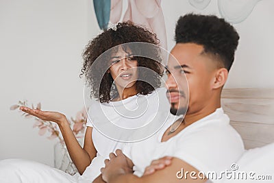 Young angry african swearing screaming couple girl guy in t-shirts lying on bed with white sheet pillow blanket indoors Stock Photo