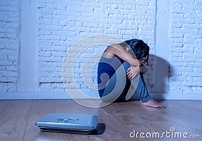 Young anorexic teenager woman sitting alone on ground looking at the scale worried and depressed in dieting and eating disorder Stock Photo