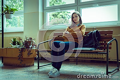 Young anxious and depressed female college student sitting in the hallway at her school. Education, Bullying, Depression, Stress. Stock Photo