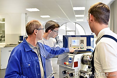 Young apprentices in technical vocational training are taught by older trainers on a cnc lathes machine Stock Photo