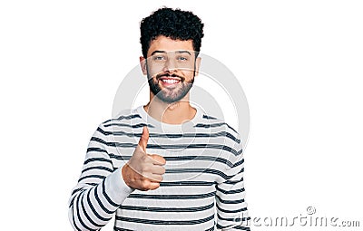 Young arab man with beard wearing casual striped sweater doing happy thumbs up gesture with hand Stock Photo