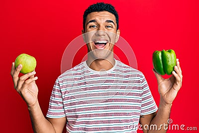 Young arab man holding green apple and pepper smiling and laughing hard out loud because funny crazy joke Stock Photo