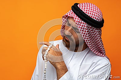 Young Arab man holding traditional beads against orange background Stock Photo
