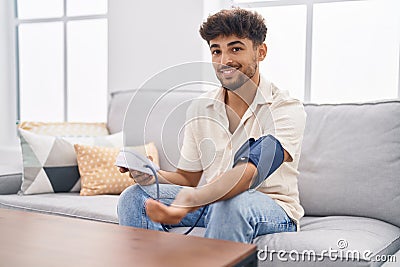 Young arab man using tensiometer sitting on sofa at home Stock Photo