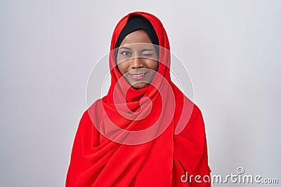 Young arab woman wearing traditional islamic hijab scarf winking looking at the camera with sexy expression, cheerful and happy Stock Photo