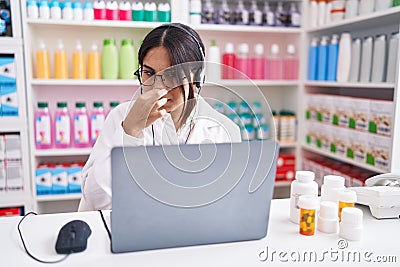 Young arab woman working at pharmacy drugstore using laptop smelling something stinky and disgusting, intolerable smell, holding Stock Photo