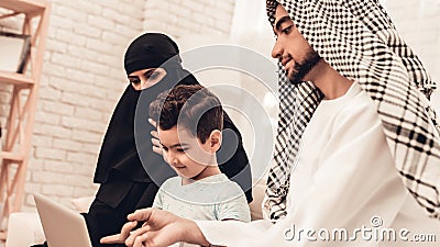 Young Arabic Family Using Laptop on Sofa at Home. Stock Photo