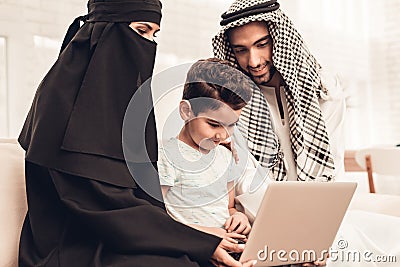 Young Arabic Family Using Laptop on Sofa at Home Stock Photo