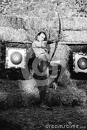 Young archer girl with bow near hay with target Stock Photo
