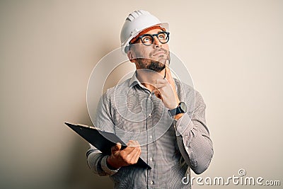 Young architect inspector man wearing builder safety helmet and using clipboard serious face thinking about question, very Stock Photo