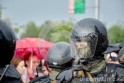 A young armed police officer watches protesters in the rain Editorial Stock Photo