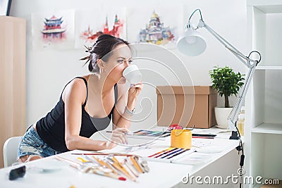 Young artist drawing watercolor picture sideview, holding cup of coffee Stock Photo