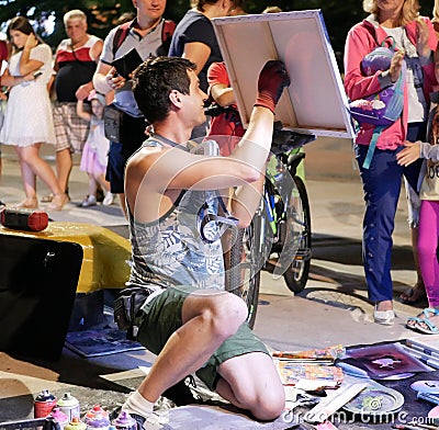 A young artist paints a picture of multicolored spray paint at night in front of everybody. A young guy in a respirator. Editorial Stock Photo