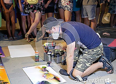 A young artist paints a picture of multicolored spray paint at night in front of everybody. A young guy in a respirator. Stock Photo