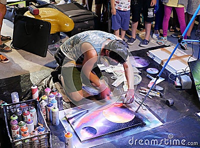 A young artist paints a picture of multicolored spray paint at night in front of everybody. A young guy in a respirator. Stock Photo