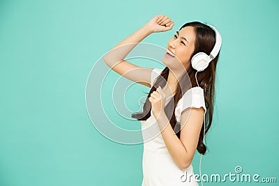 Young Asian beauty woman dancing and listening music with headphones on smartphone on green background. Stock Photo