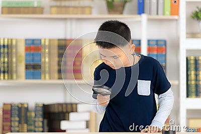 Young Asian boy smiling and hold magnifying glass the library is Stock Photo