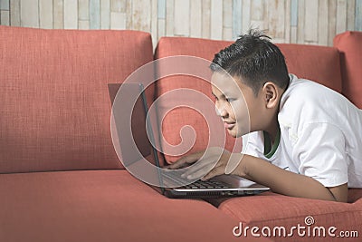 Young asian boy smiling using laptop computer on a sofa at home. Stock Photo