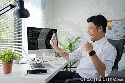 Young Asian businessman in casual wears excited, shouting, and a joyful expression in the office as he looks at trading charts on Stock Photo