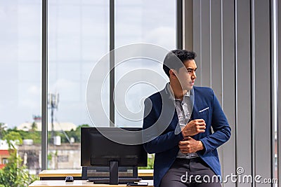 Young Asian businessman sit on a desk in a comfortable position. And the hands were buttoned up on the sleeves Stock Photo