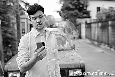 Young Asian businessman using mobile phone against rusty old car Stock Photo