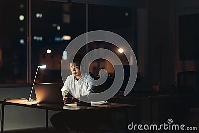 Young Asian businessman working overtime in a dark office Stock Photo