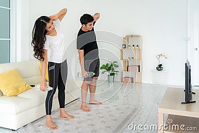 Young Asian couple doing High-intensity interval training together and looking TV at home, man and woman working out together Stock Photo