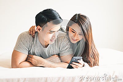 A young Asian couple plays a telephone in the bed in the bedroom. Stock Photo