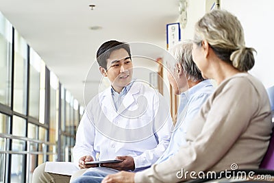 Young asian doctor talking to senior couple patients in hospital hallway Stock Photo