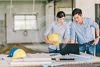 Young Asian engineer couple work together using notebook computer at building construction site. Civil engineering meeting concept Stock Photo