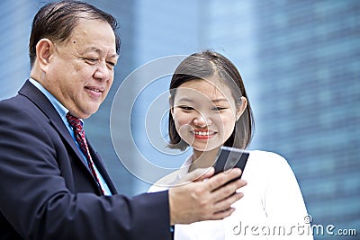 Young Asian female executive and senior businessman using smart phone Stock Photo